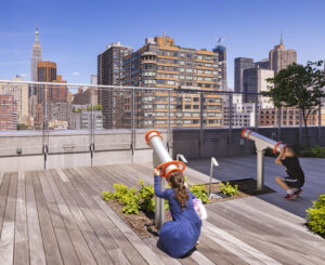 Photograph of an outdoor terrace at NYU Hassenfeld Children's Hospital showing a pair of large kaleidoscopes with children looking through them at the NYC skyline