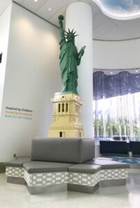 Photograph of the interior of NYU Hassenfeld Children's Hospital showing a tall Lego Statue of Liberty above a bench in a waiting area
